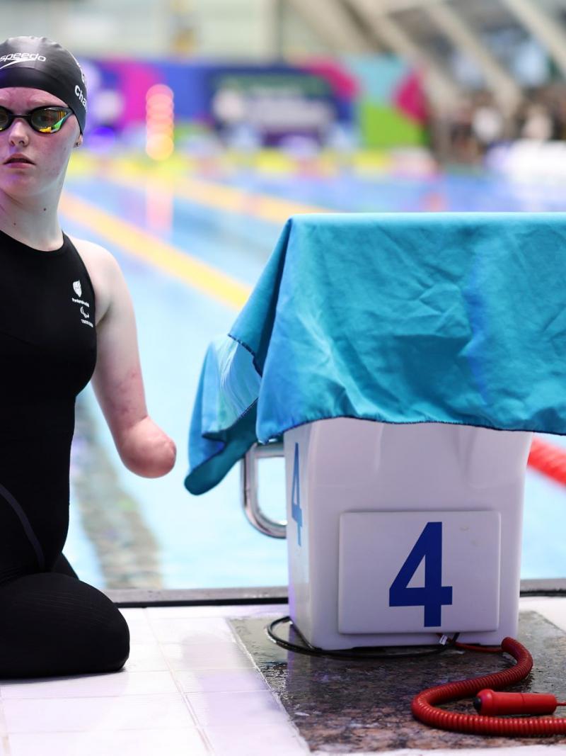 A female Para swimmer next to the starting block of a swimming pool