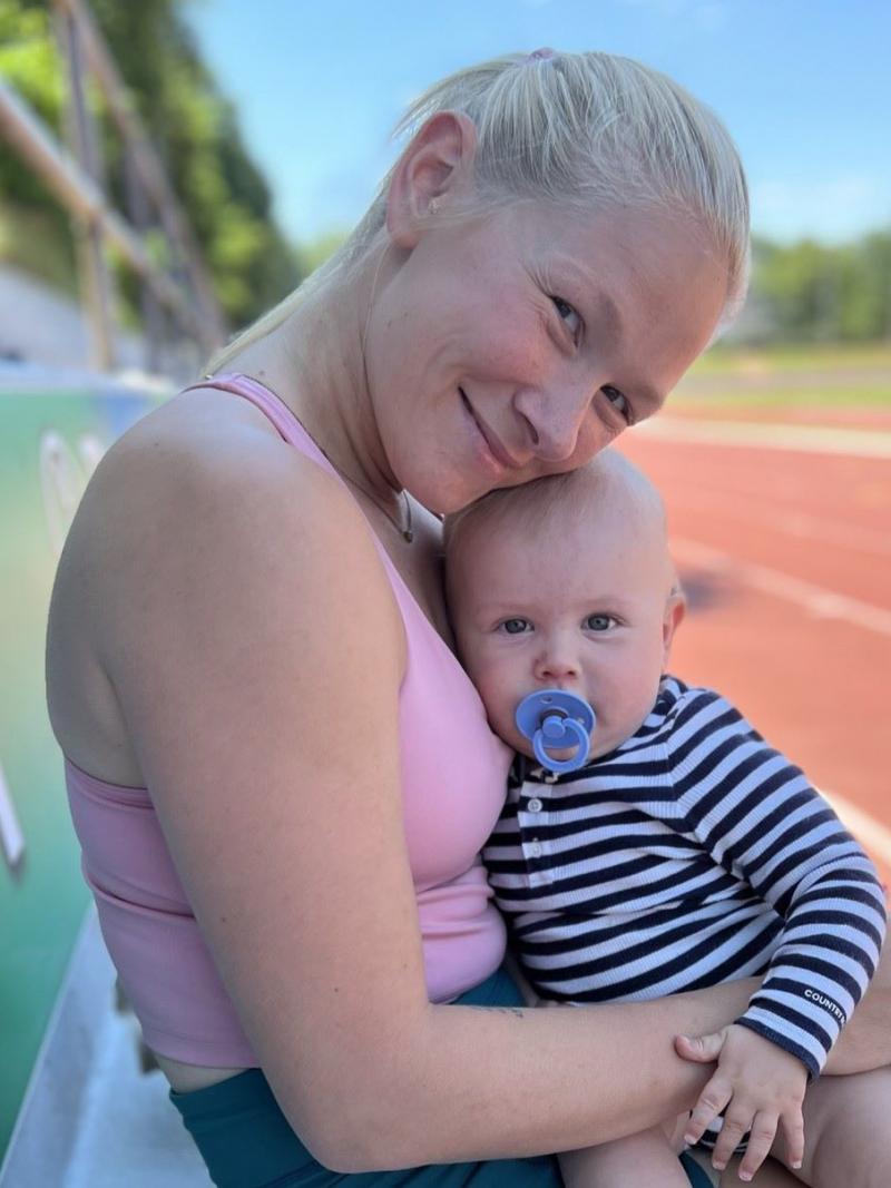 A female athlete sits by the tracks and holds a baby boy.
