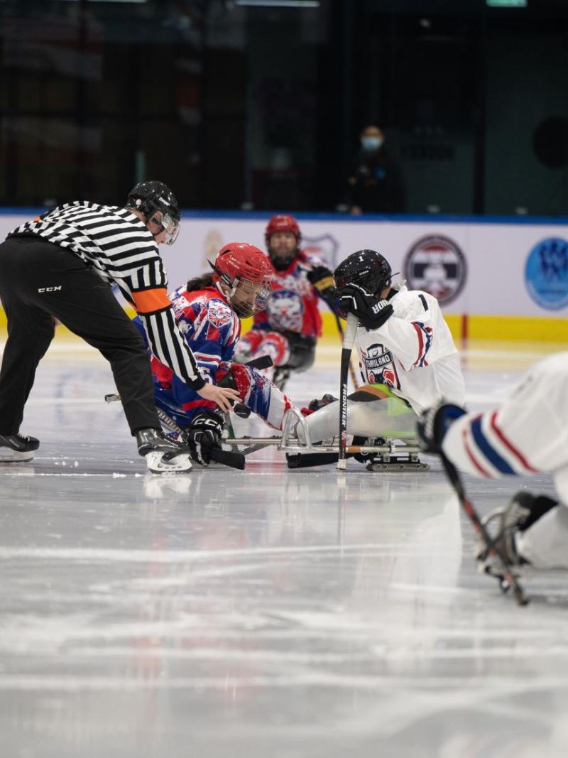 A Para ice hockey referee and two players on a face-off