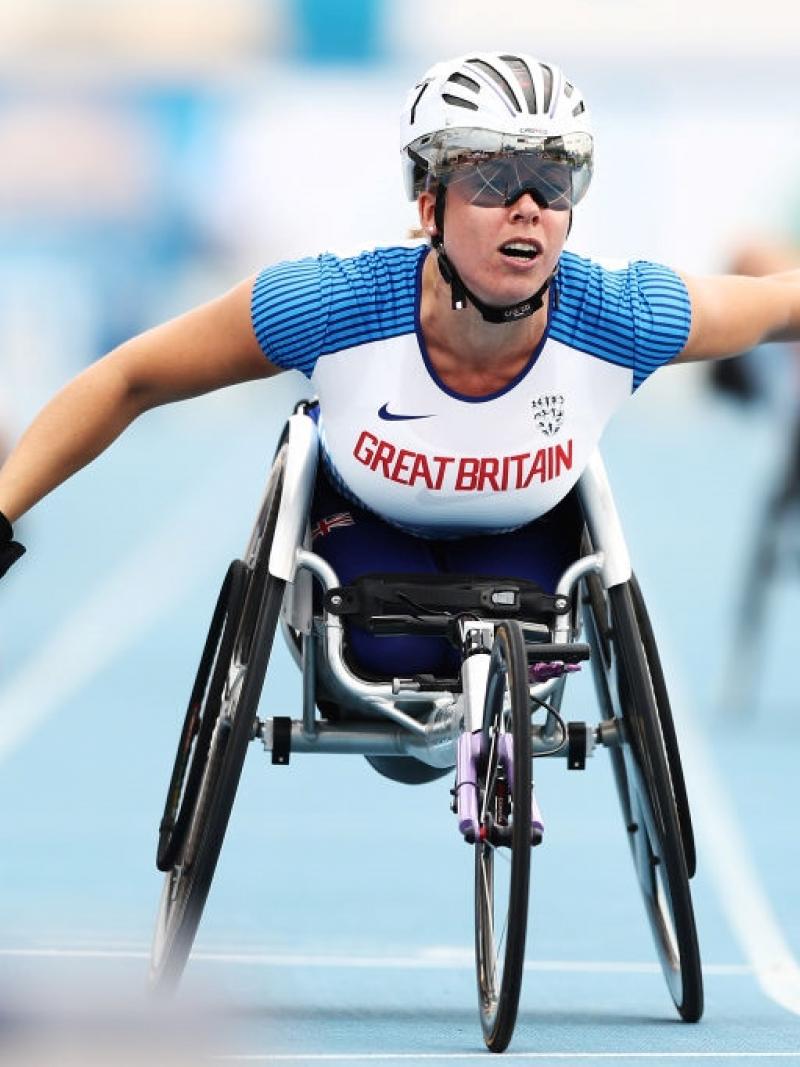 A female wheelchair racer crossing the finish line ahead of two competitors