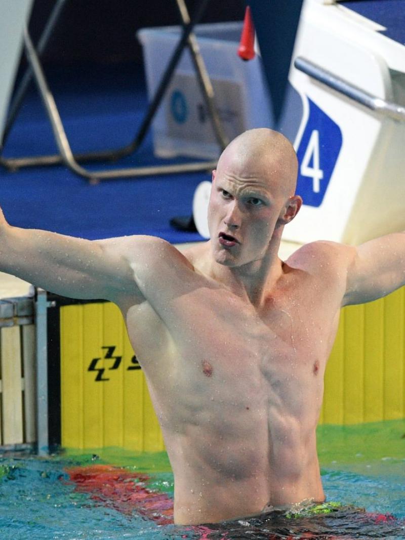 A male swimmer open his arms to celebrate in the pool