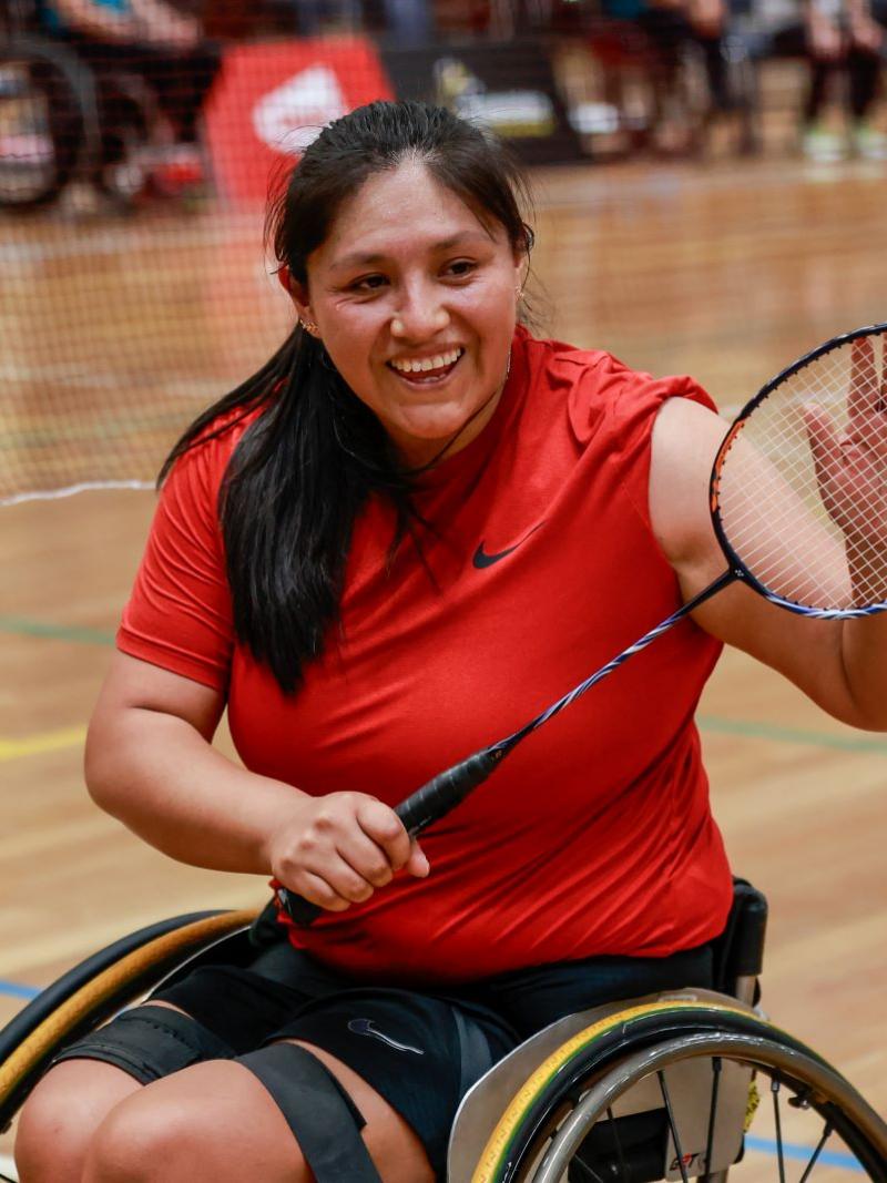 A female Para badminton player, who competes in a wheelchair, holds a racquet and smiles
