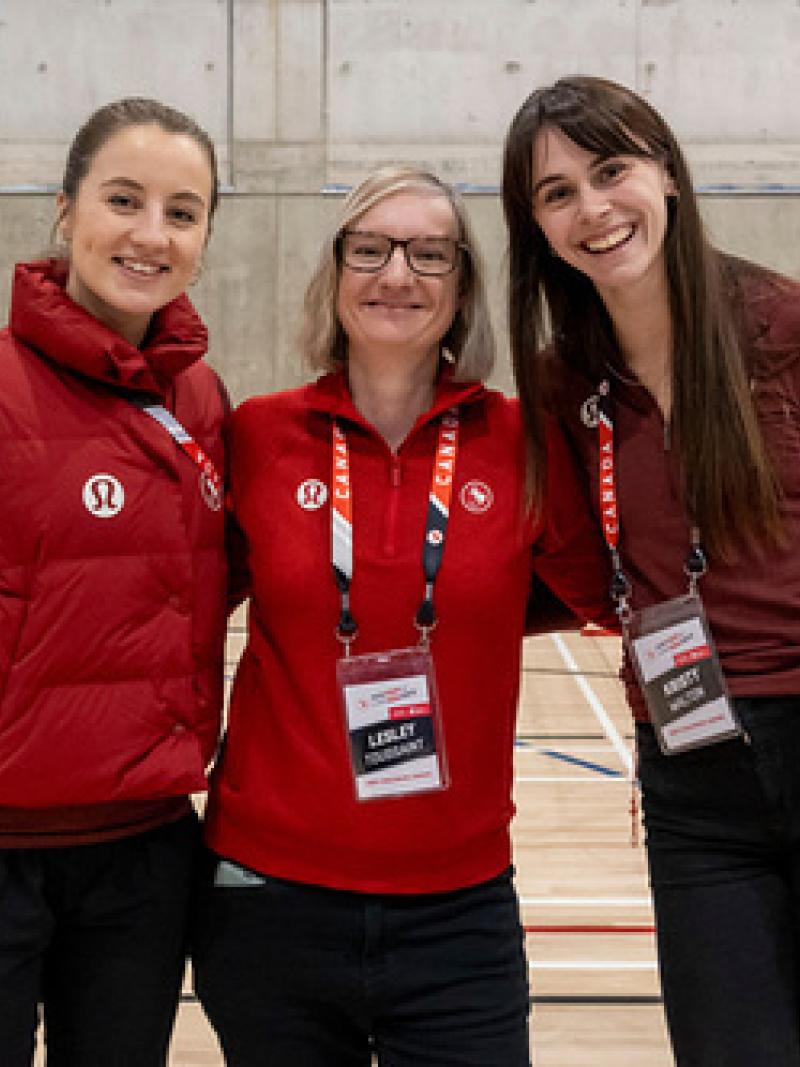 Three women wearing Canada's red uniforms pose for a photo