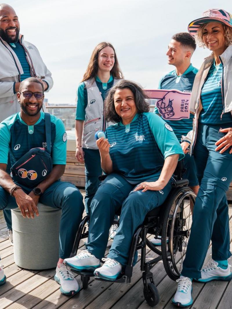 Six male and female volunteers pose for a photograph wearing the Paris 2024 volunteer uniform.