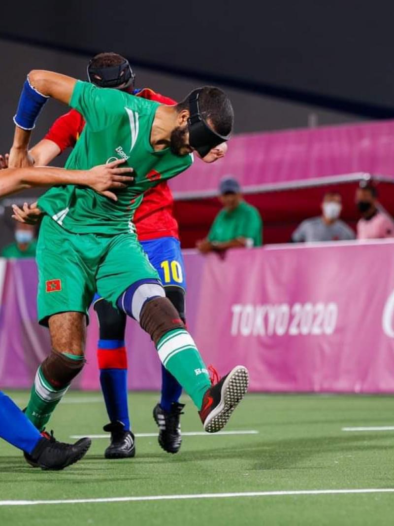 A male blind football player wearing a green uniform runs past two players