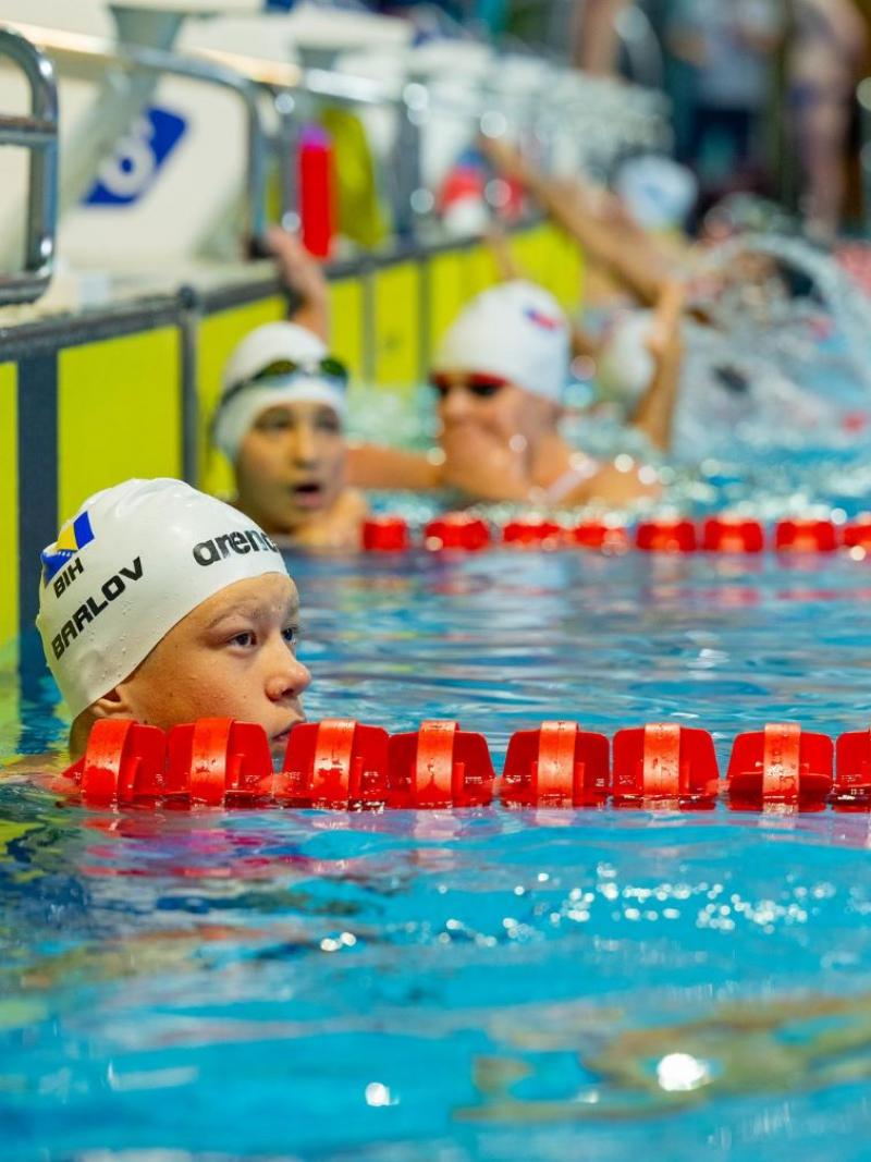 A male swimmer in a swimming pool lane with other swimmers in the background