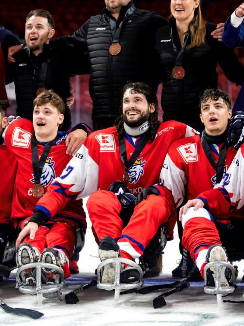 A group of Para ice hockey players with a group of standing people behind them