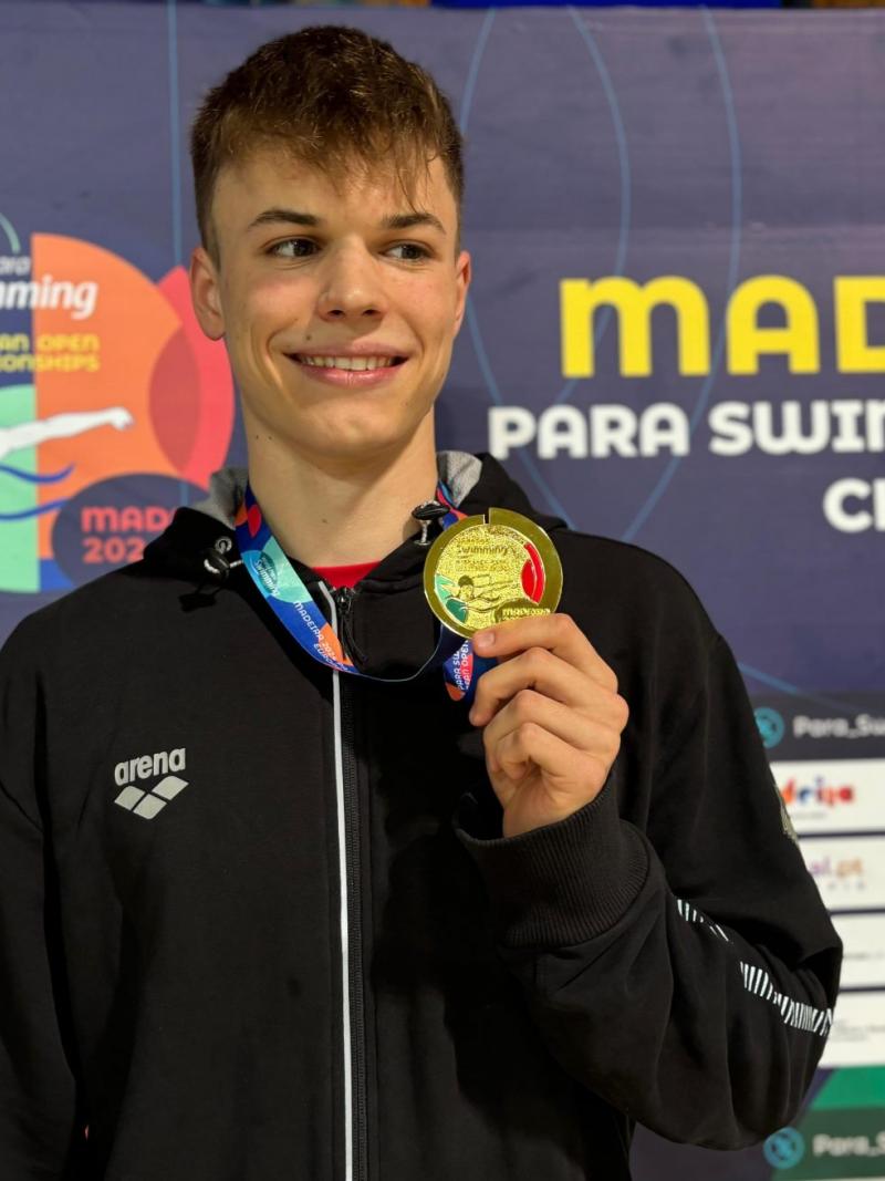 A man showing his gold medal on a podium