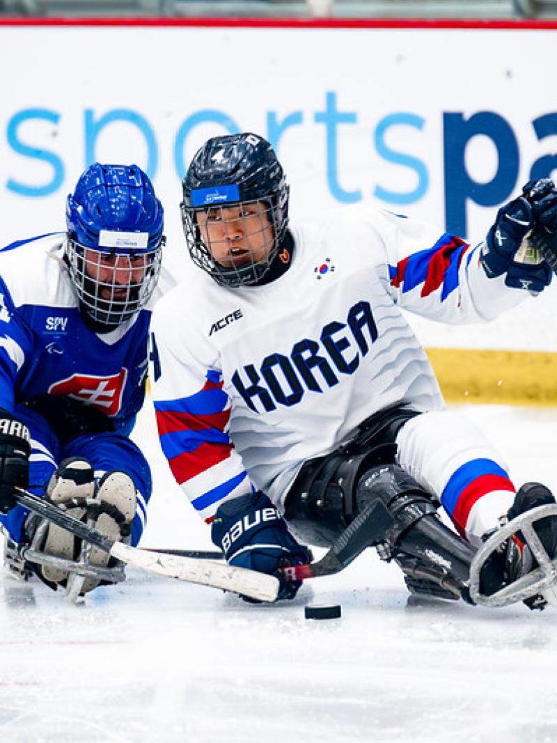 Two Para ice hockey players trying to reach the puck