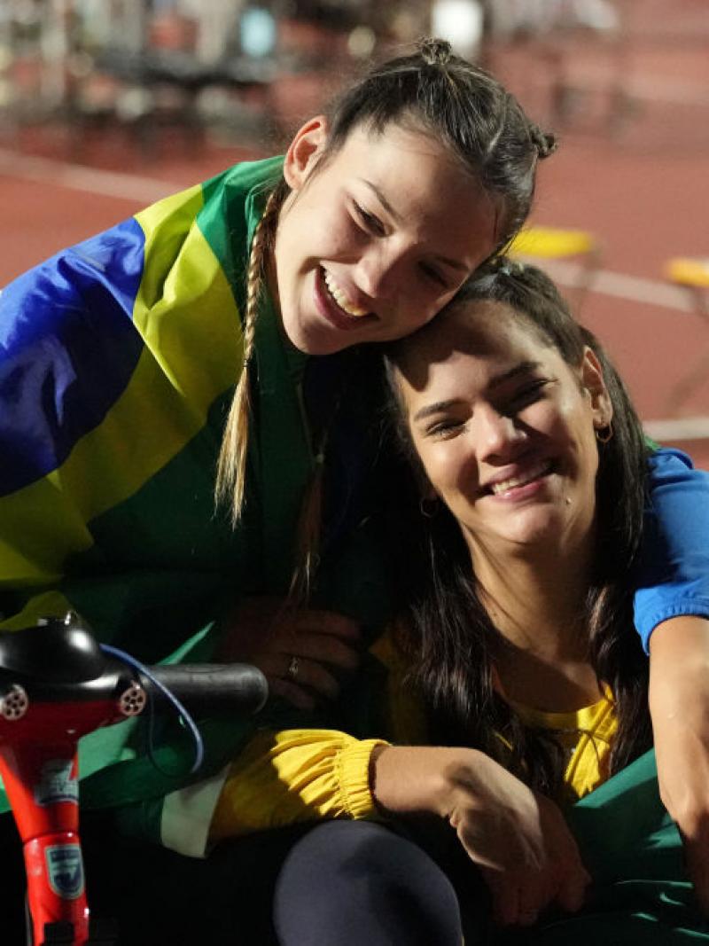 A woman in a wheelchair hugging another woman sitting on the ground