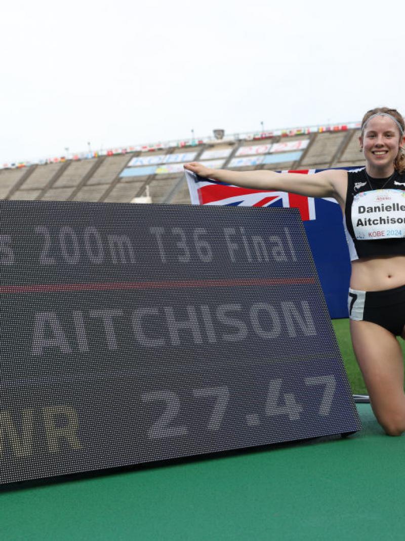 A young female athlete posing for a picture next to a screen showing a world record