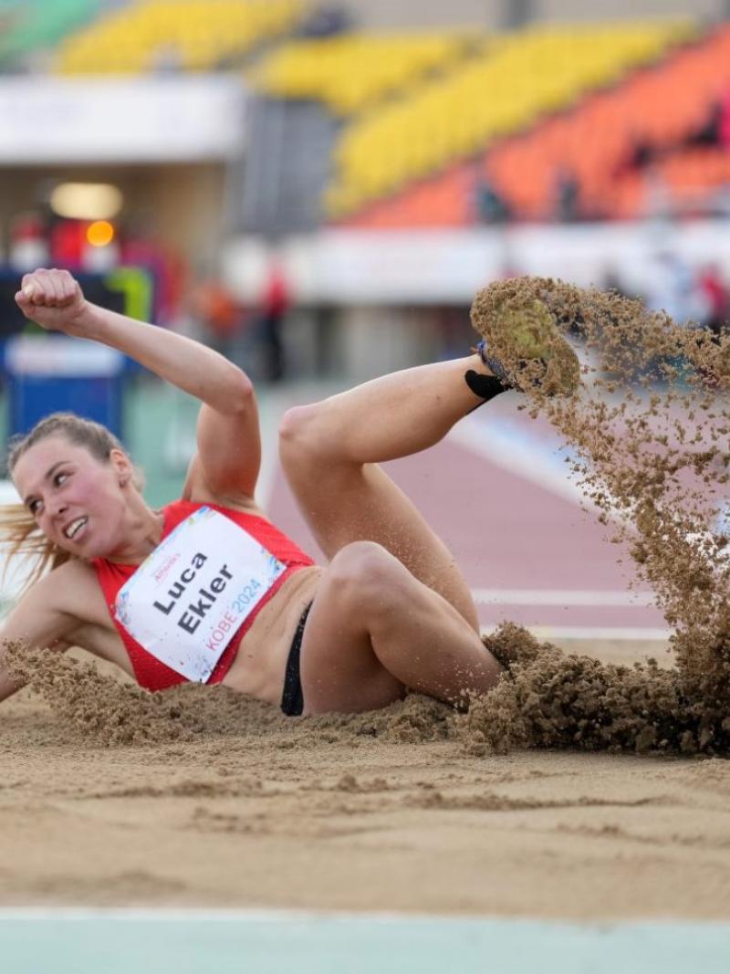 A female athlete landing in the sand in a long jump event
