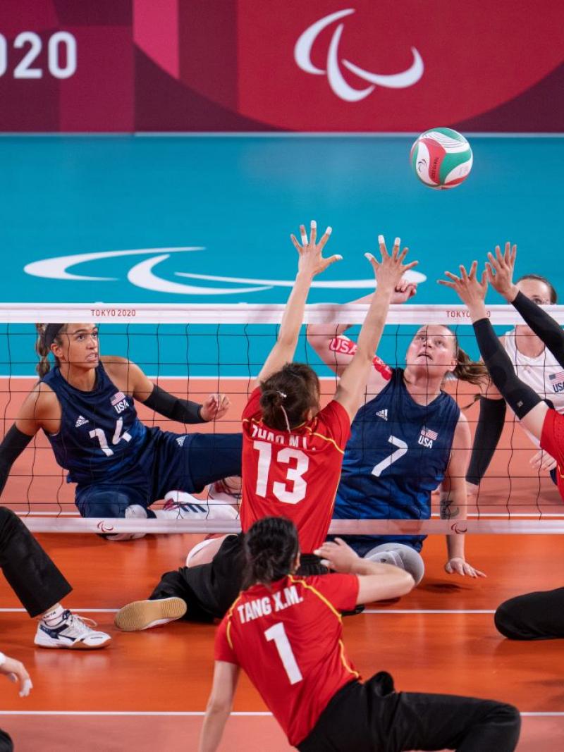 Two sitting volleyball athletes try to block the ball during a match.