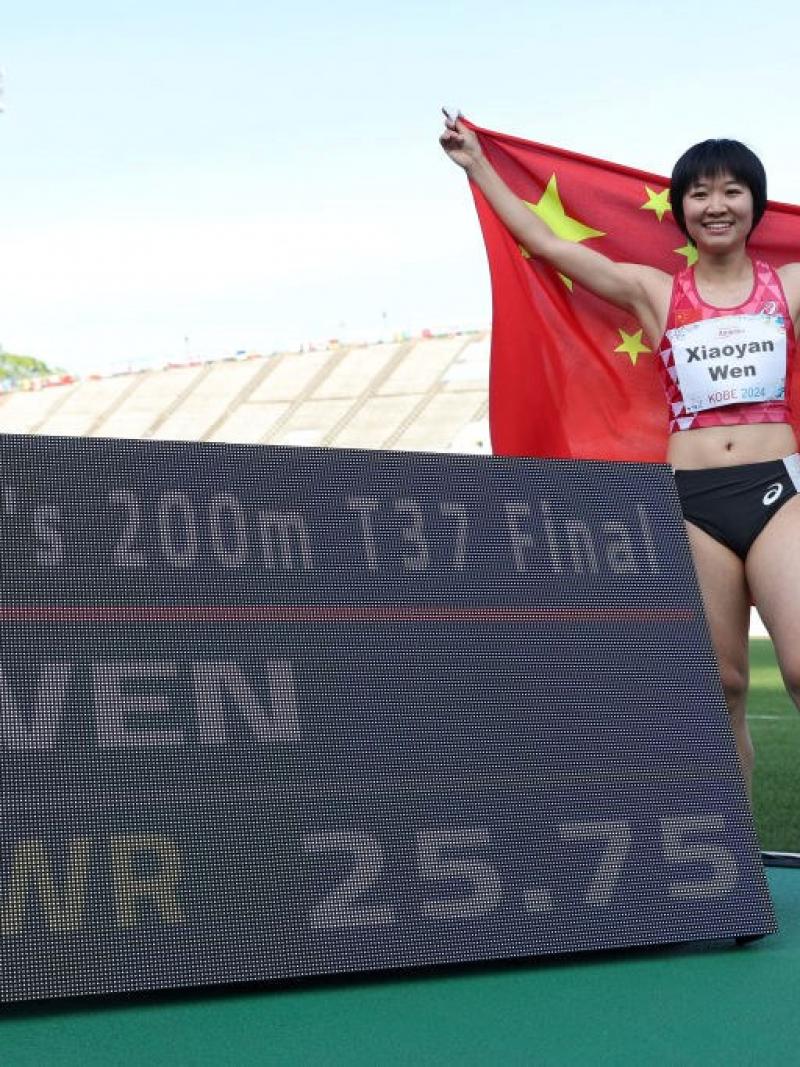 An athlete with the Chinese flag posing next to a scoreboard