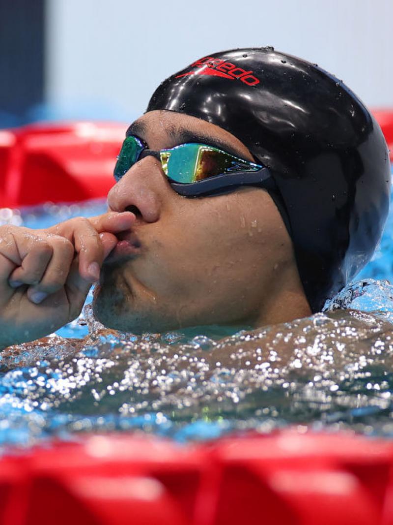 A male Para swimmer holds his hands to his lips in the pool after a competition