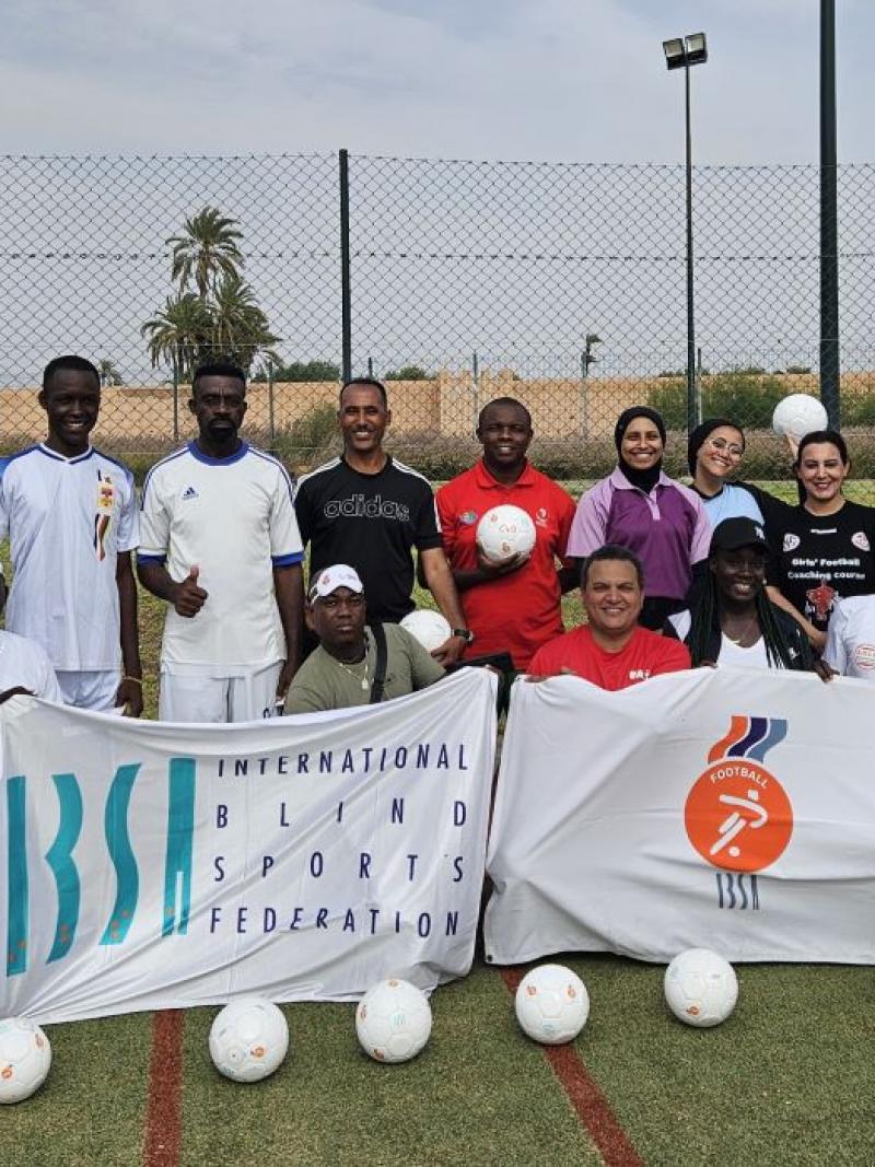 Sixteen people pose for a photograph with IBSA flags