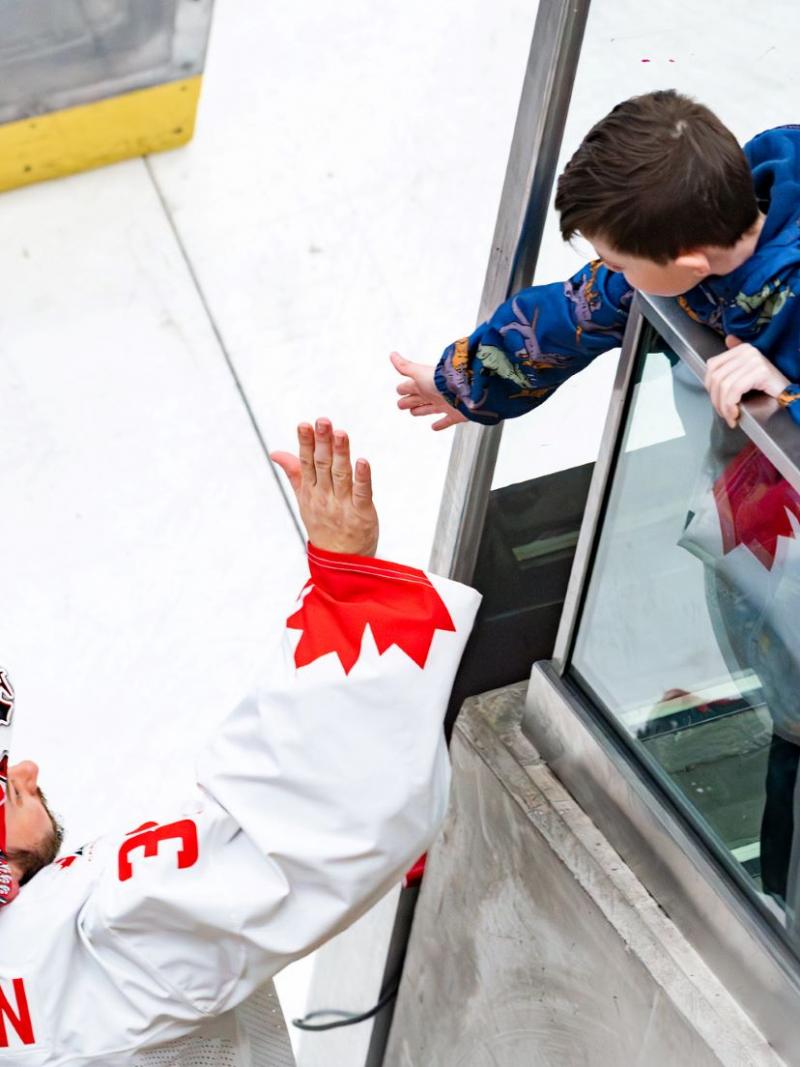 A hockey goaltender high-fiving a young fan in a rink