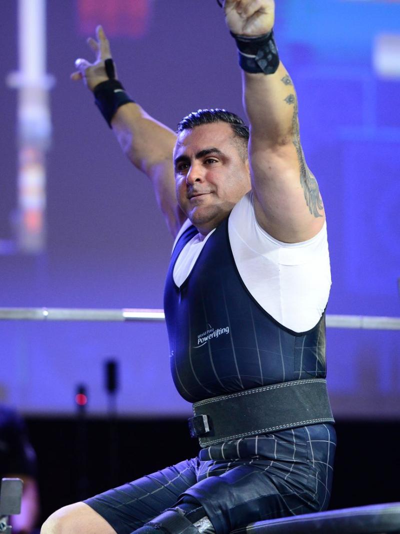 Para powerlifting athlete Hadi Darvishpoor sits in front of the weight and raises both arms.