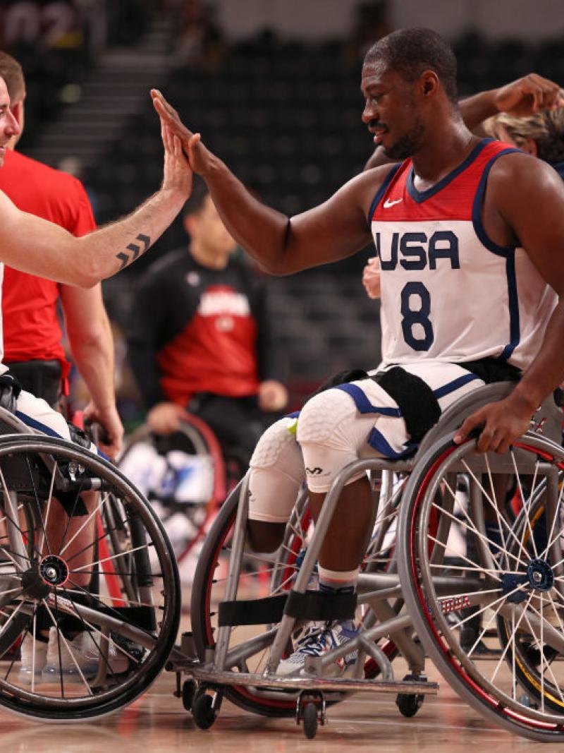 Two male wheelchair basketball players do a high-five to celebrate a victory