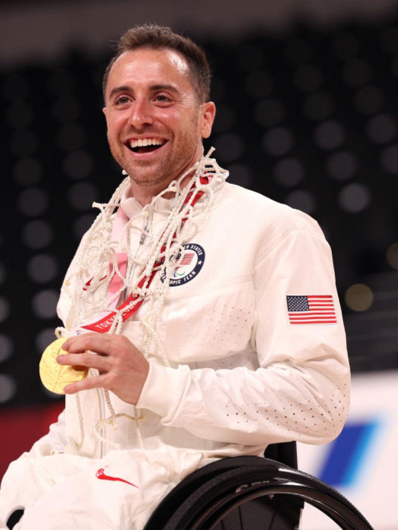 A male wheelchair basketball player posing for a photo while holding a gold medal. 