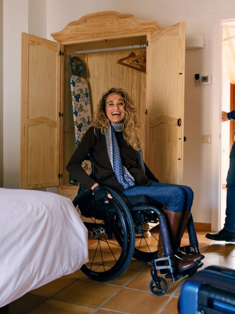 A female wheelchair user enters a bedroom and smiles