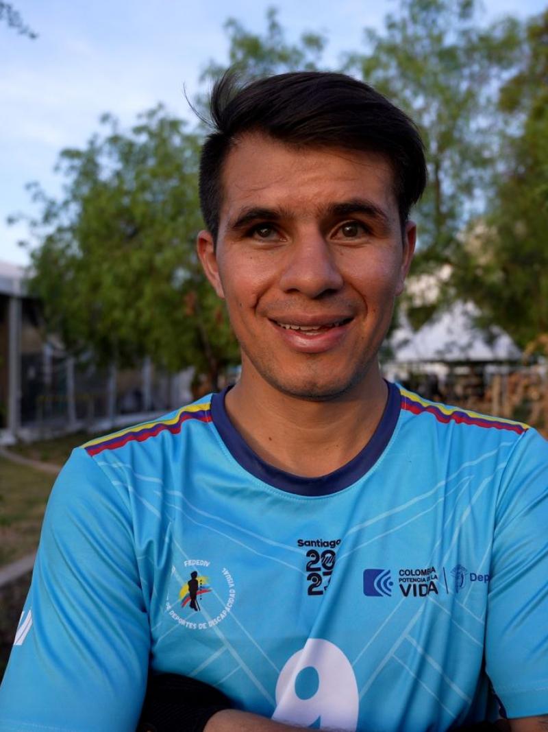 Jhon Gonzalez, a blind football player from Colombia, is standing outdoors wearing a blue uniform, crossing his arms