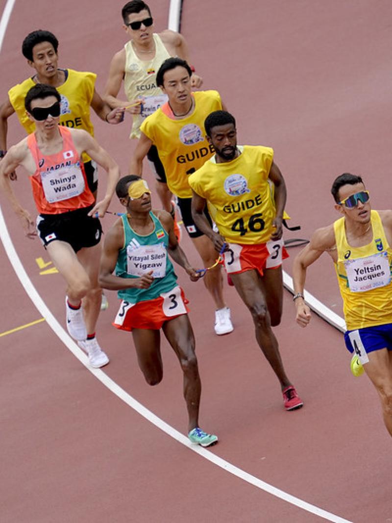 A runner and his guide ahead of three other runners with guides in a race