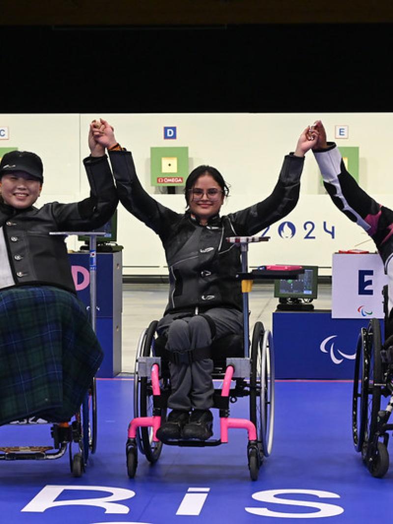 Three women in wheelchairs holding hands in a shooting range