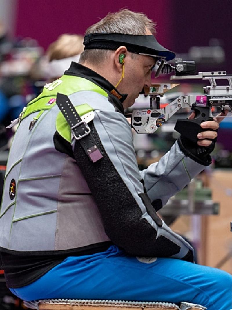 A male athlete competing in a shooting Para sport range in front of other athletes