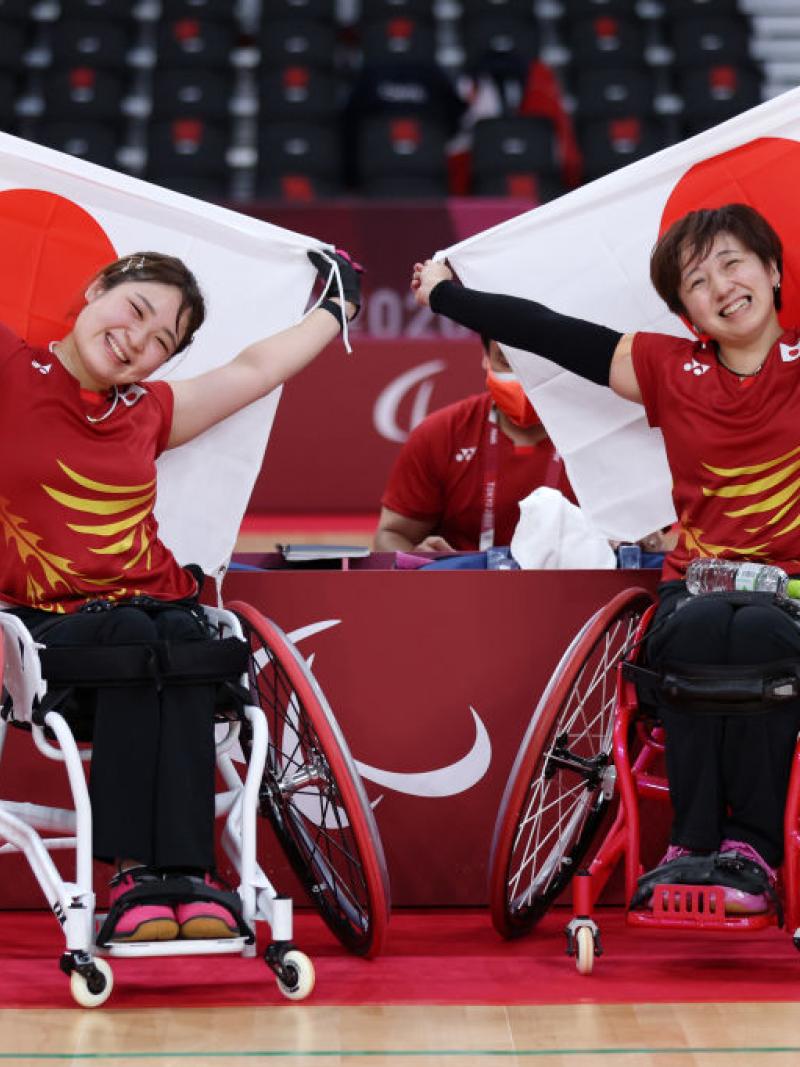 Sarina Satomi and Yuma Yamazaki are smiling as they sit and hold the Japanese flags after winning gold at Tokyo 2020