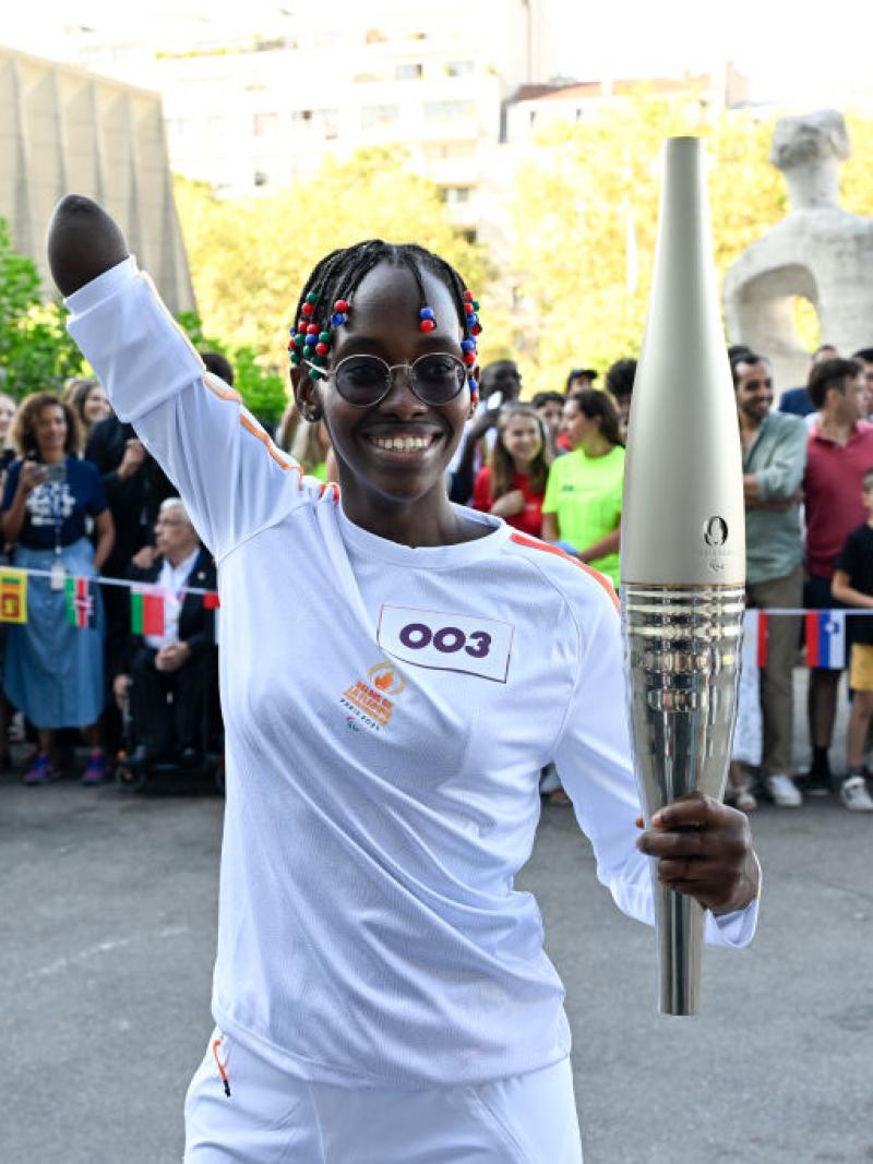 Para swimmer Husnah Kukundakwe holding the Paris 2024 torch and smiling with her arm in the air 