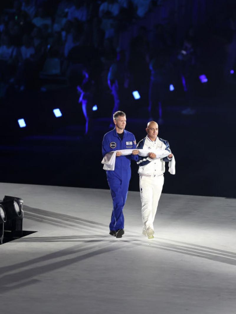 Two men carry a rolled up Paralympic flag across a stage at the Opening Ceremony