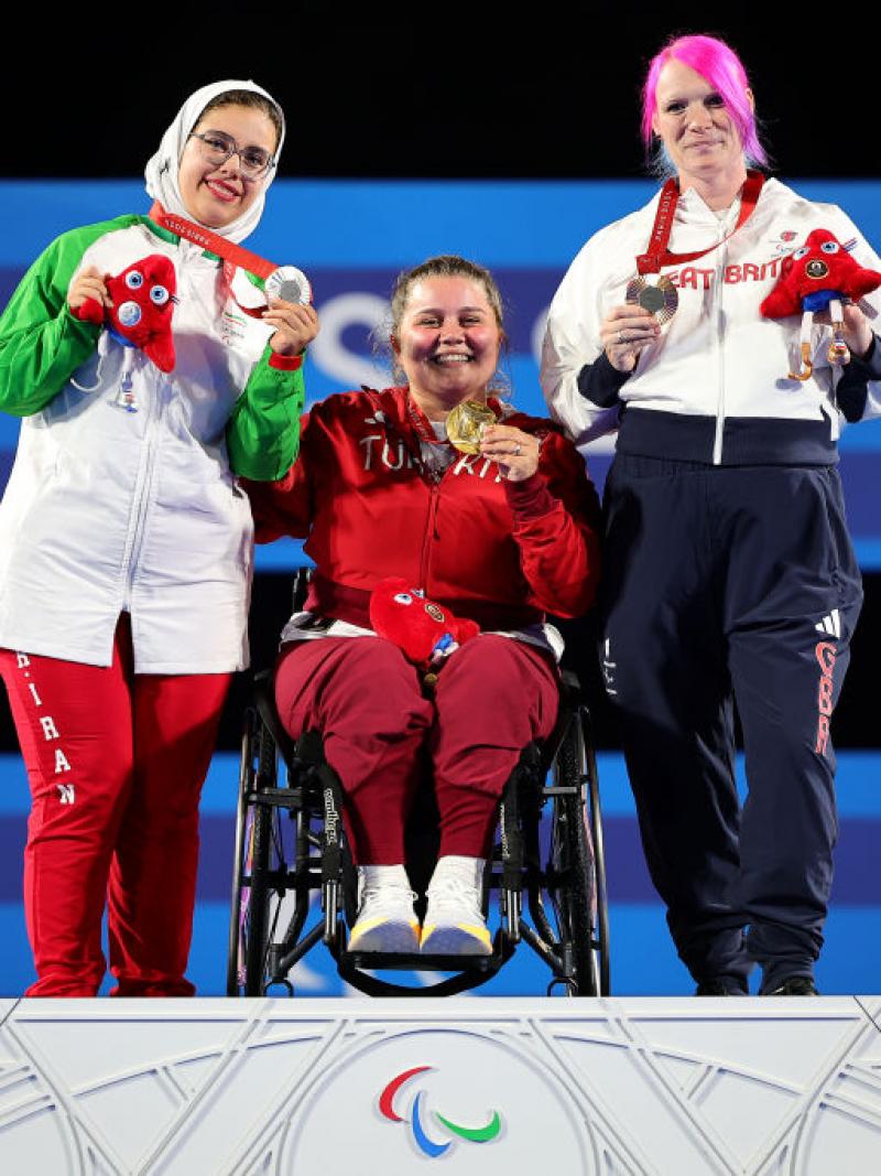 Three women pose on a podium, holding their medals