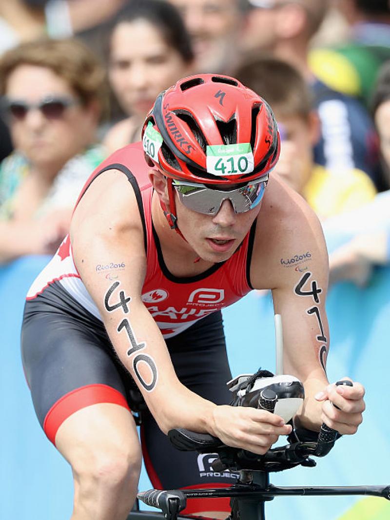 Stefan Daniel in a red Canada kit leans forward on his bike in front of a crowd at Rio 2016