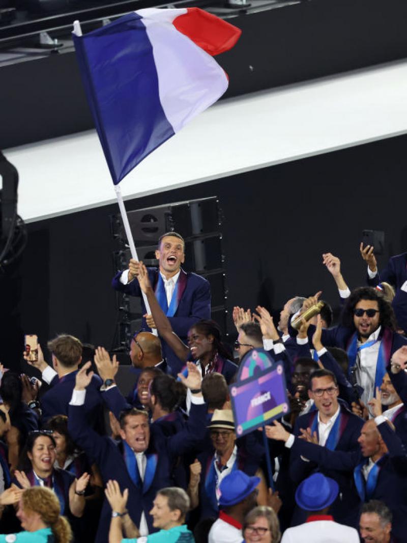 French athletes taking part in the Paris 2024 Parade of Nations. A male athlete is waving the French flag.