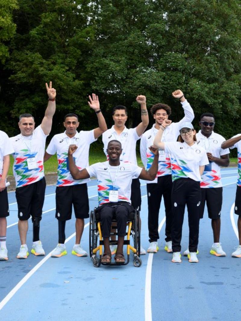 Ten people - eight athletes and two guide runners - pose for a photo on a track. They are wearing watching uniforms
