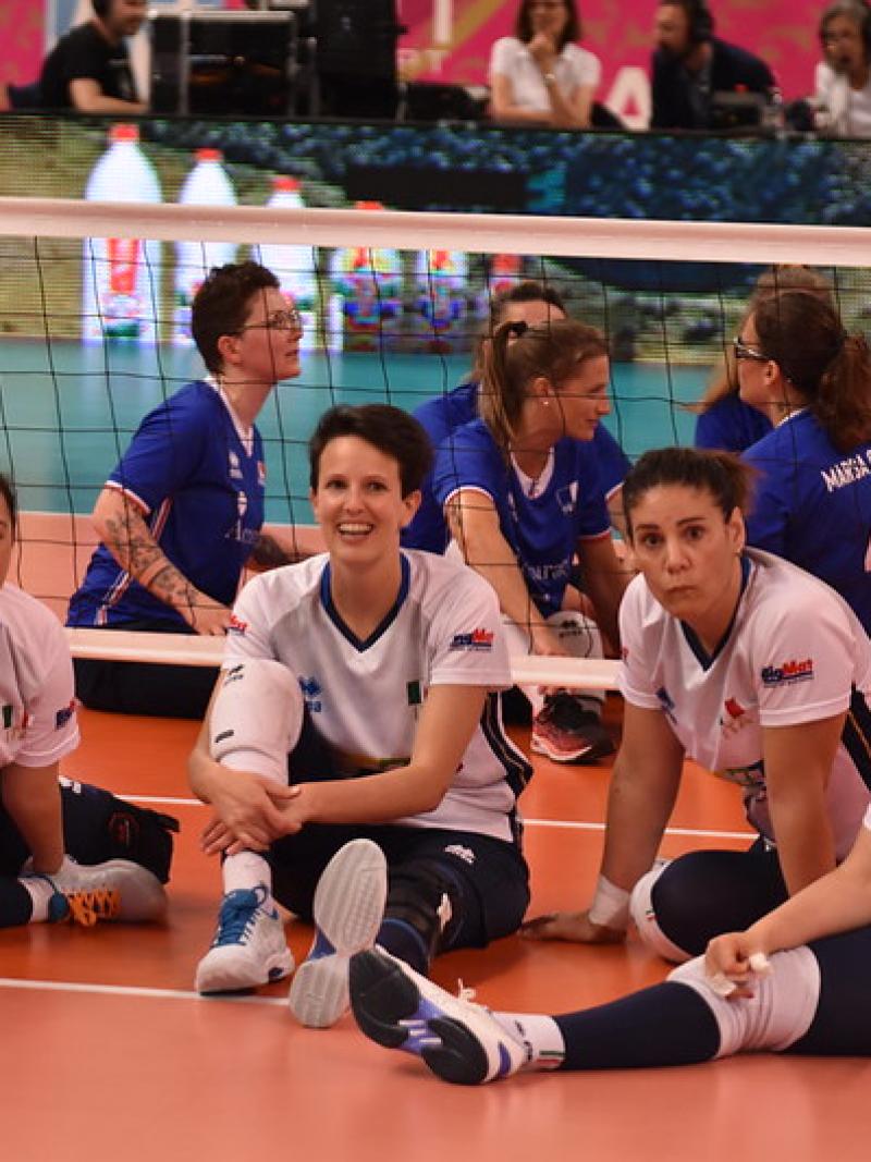 Six female sitting volleyball players sitting on the court and smiling