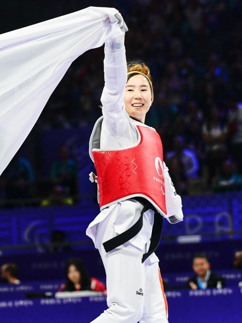 Zakia Khudadadi, a female Para taekwondo athlete, runs while holding the Paralympic flag with her right hand