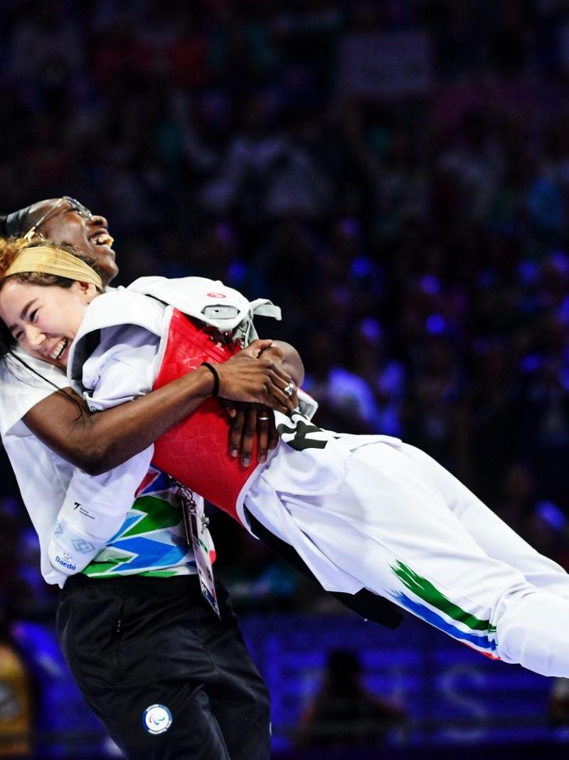 Coach Haby Niare lifts up Zakia Khudadadi, a female Para taekwondo athlete, to celebrate