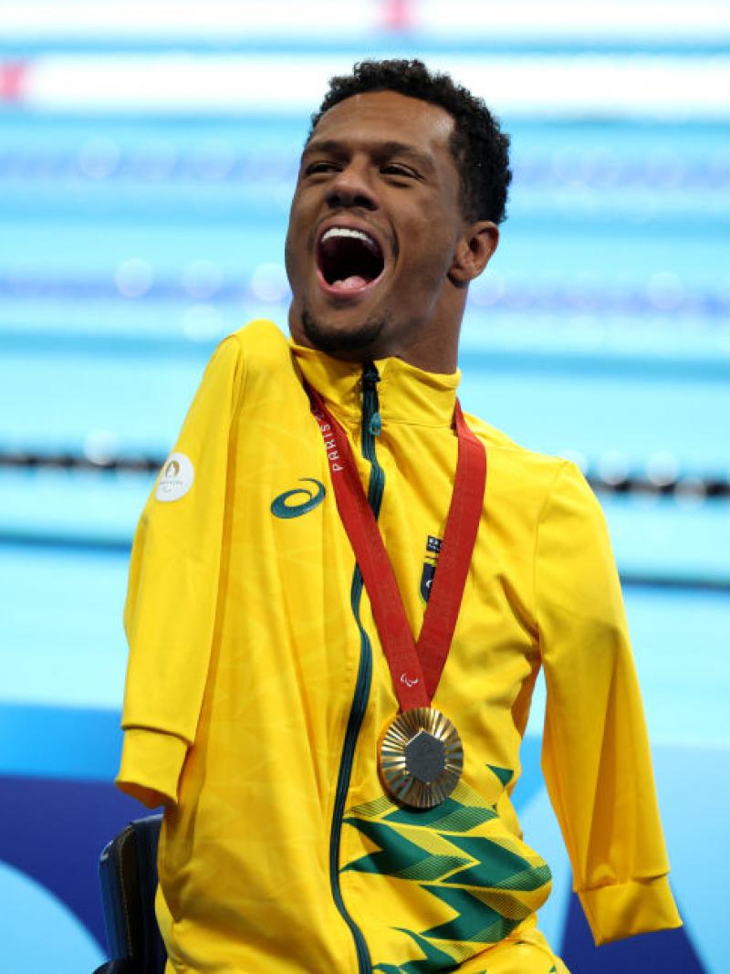 A man in a yellow jacket wears a gold medal and happily yells