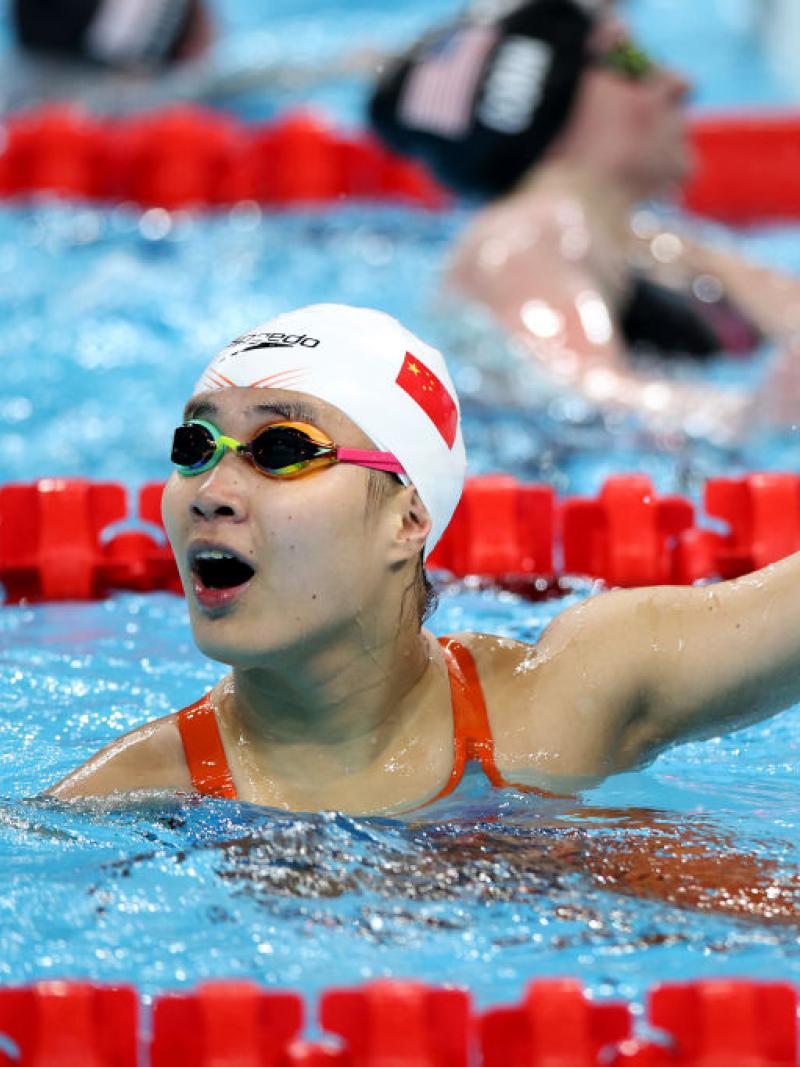 woman in goggles and speedo cap holds on to the edge of the pool and looks up shocked