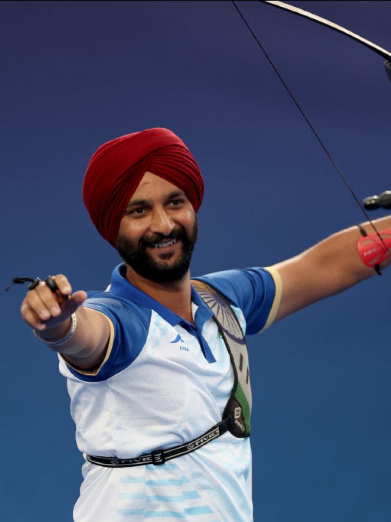 A man raises both arms in the air, carrying an archery bow in one hand