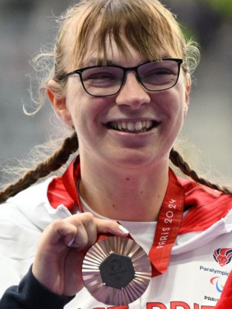 Para athlete Anna Nicholson holds up a bronze medal and smiles 