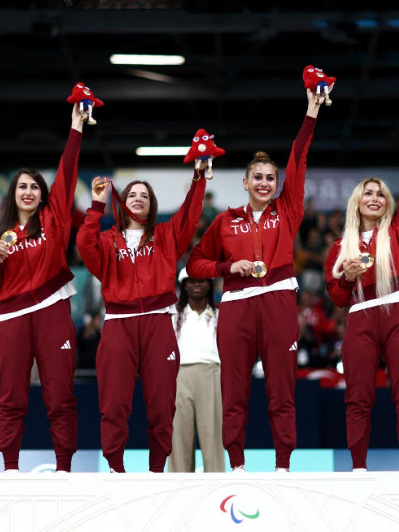 six women in red Turkiye uniforms hold up the Paris 2024 mascot and their gold medals with smiles on their faces