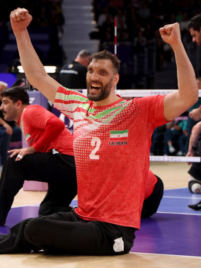 A sitting volleyball player raises his arms in celebration while on the volleyball court