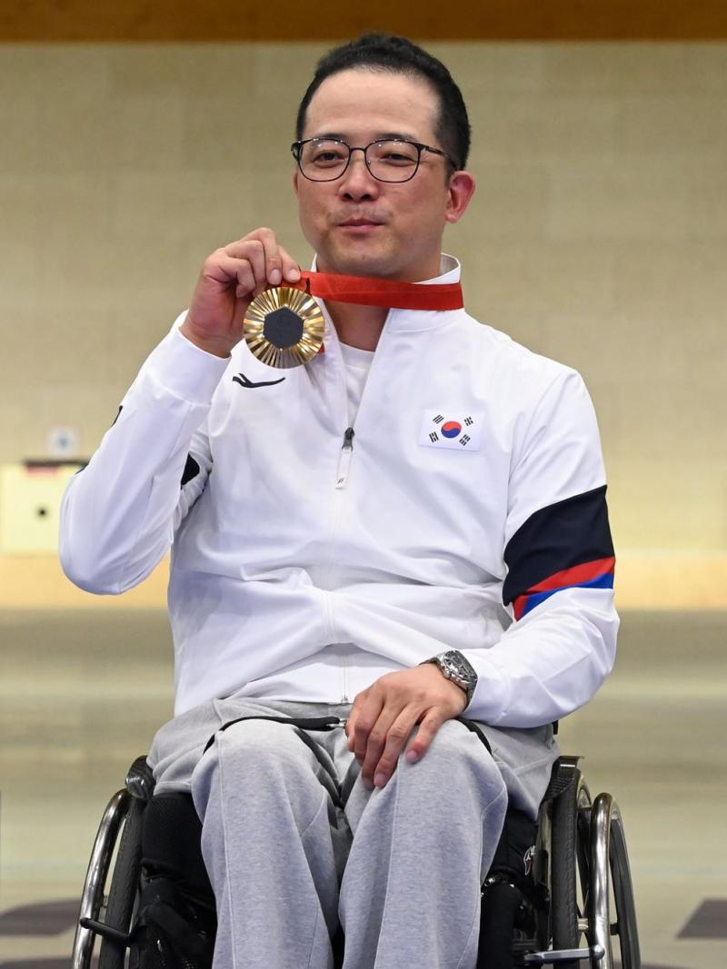 A man in a wheelchair showing his gold medal in a shooting range