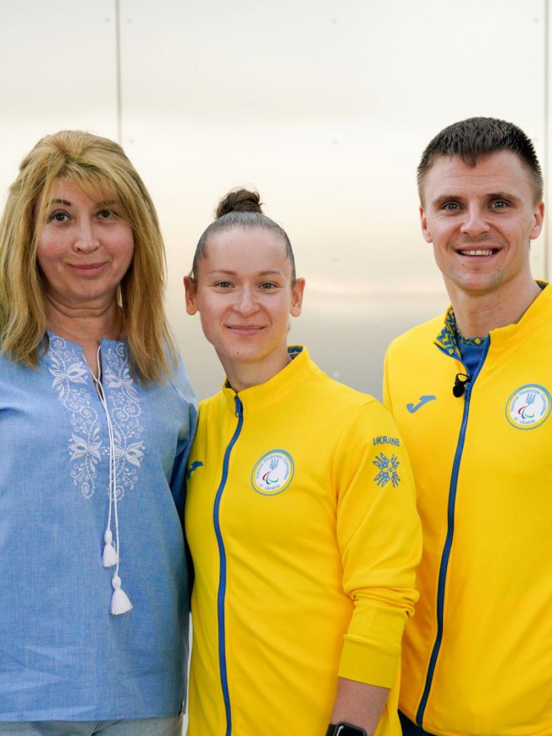 Oksana Kozyna and Oleksandr Chyrkov standing with their teacher and smiling 
