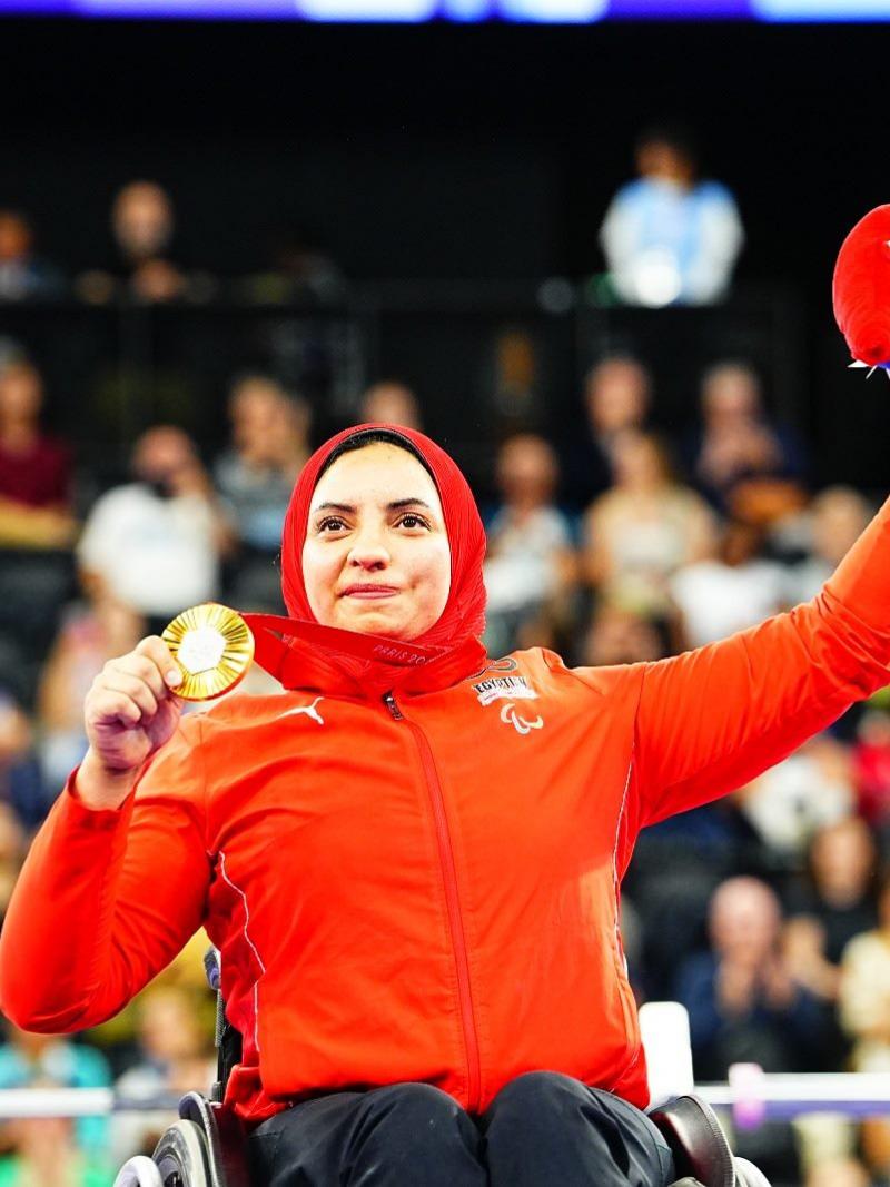 A woman in a wheelchair showing her medal to the public in an arena