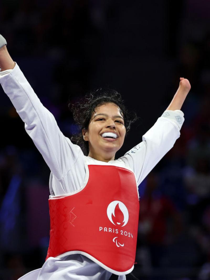 A female Para taekwondo athlete celebrates by holding Nepal's flag on the taekwondo mat