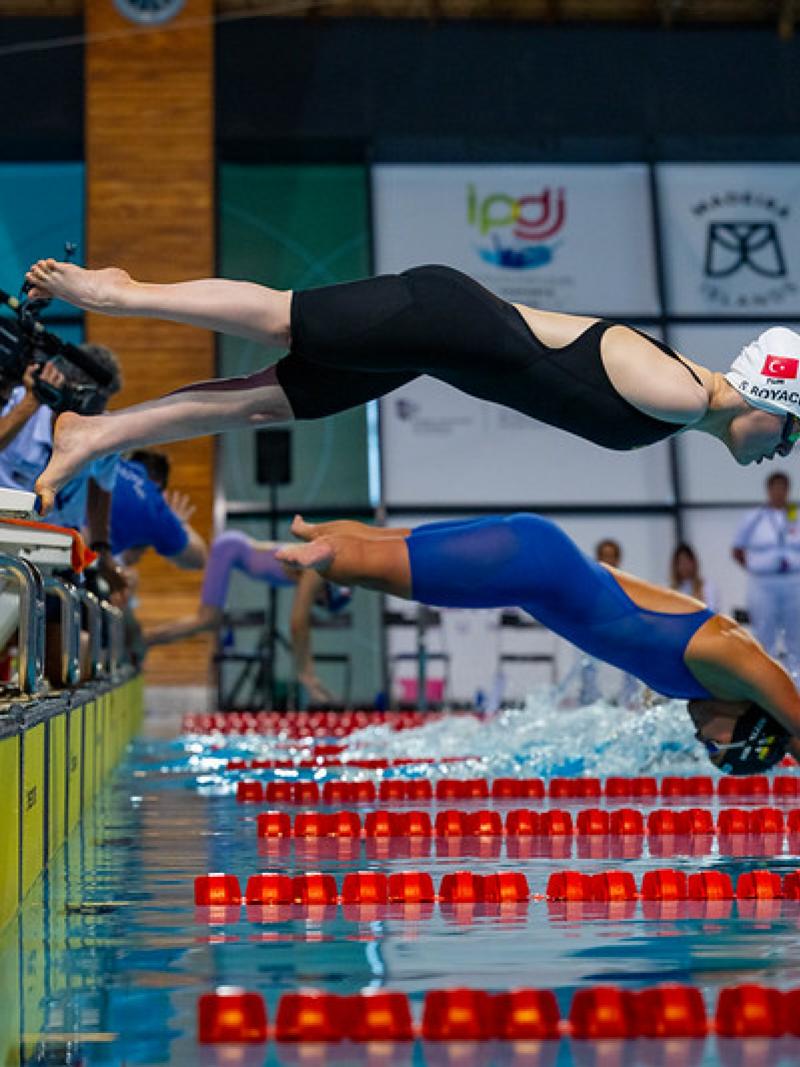Two female Para swimmers jump in the water in a swimming pool